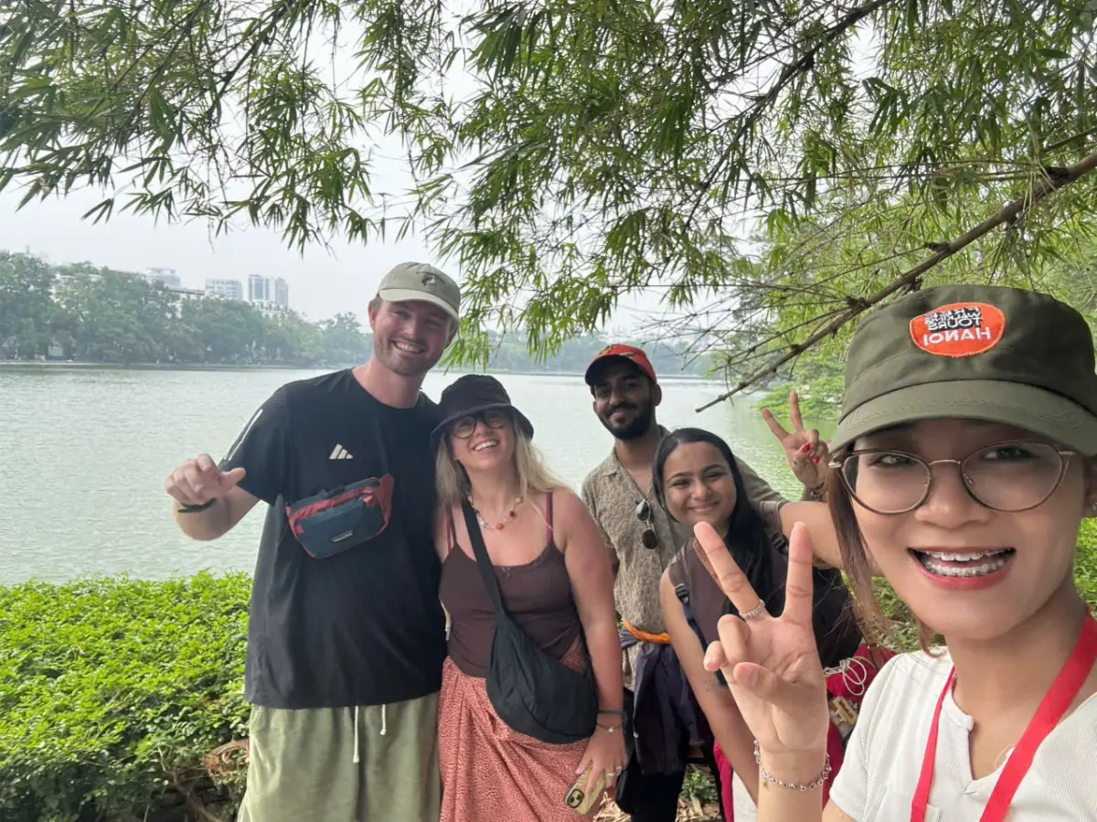 Walking tour group selfie with guide Hannah under willow trees beside Hoan Kiem Lake, Hanoi.