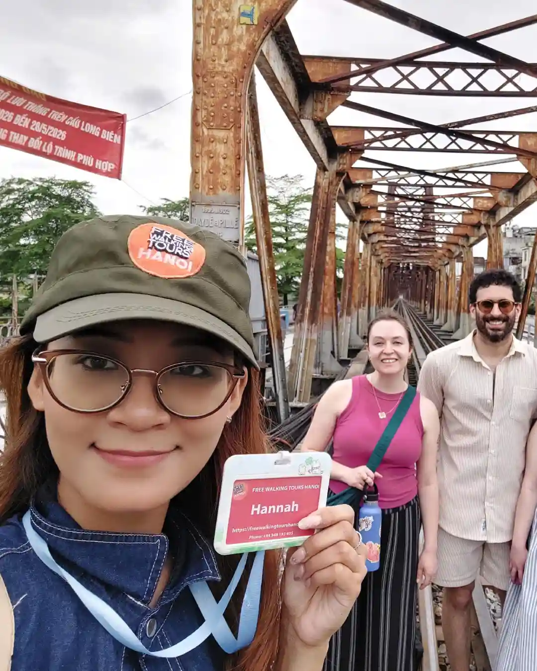 Guide Hannah on rusted railway tracks of Long Bien Bridge with travellers behind her.
