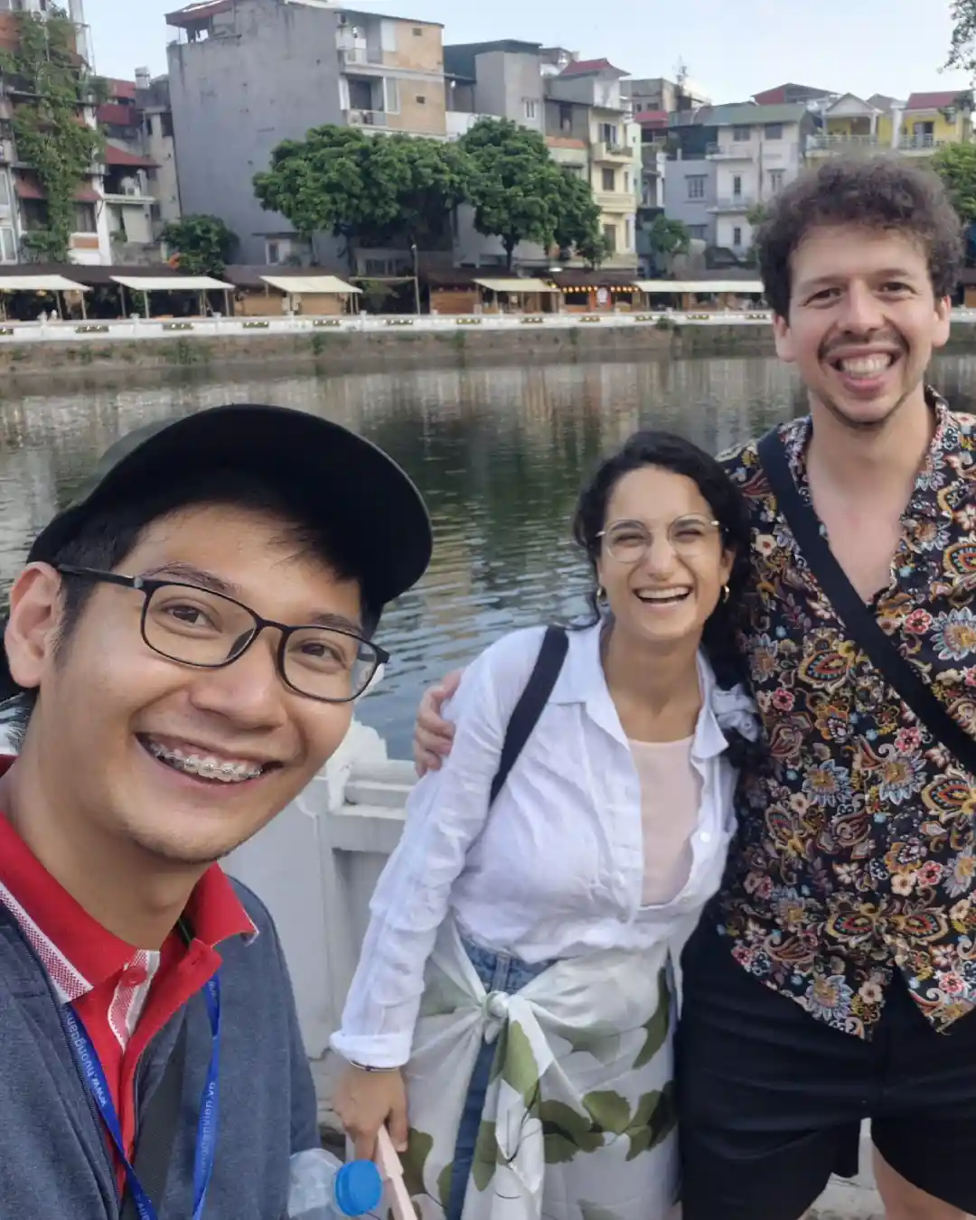 Guide and travellers beside a calm Hanoi lake with floating restaurants at dusk.