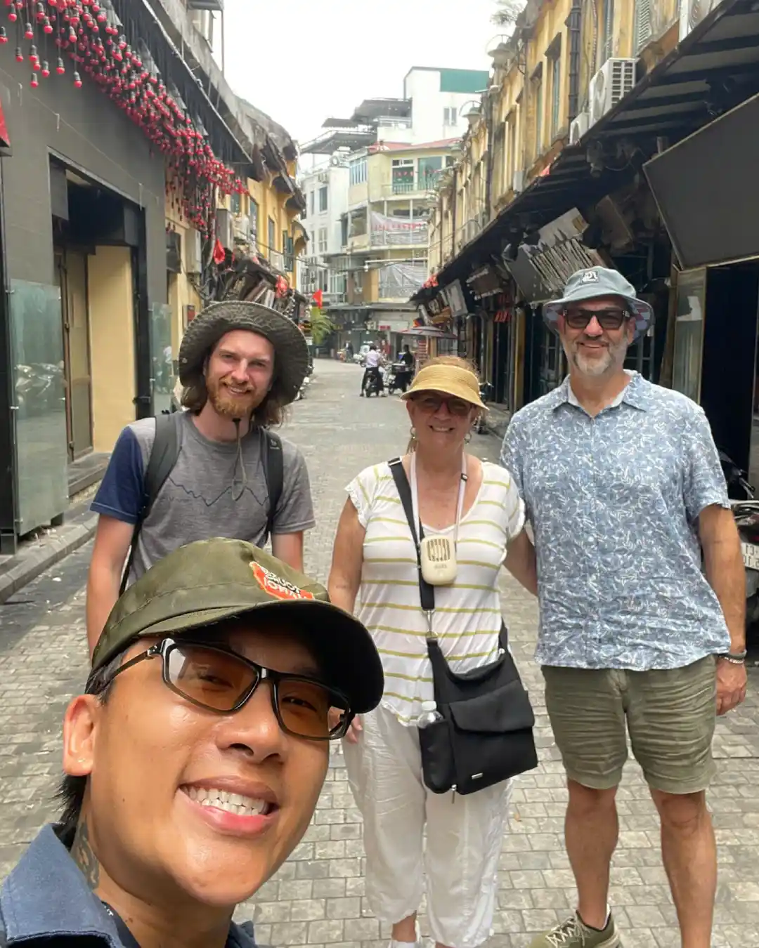 Guide in Free Walking Tours Hanoi cap with travellers on a cobblestone Old Quarter street.