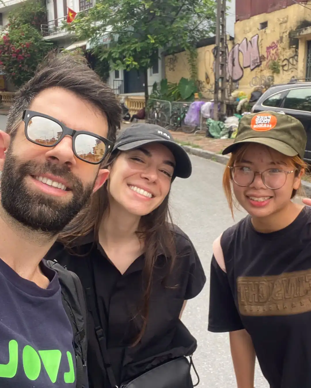 Guide with travellers on a Hanoi side street with bougainvillea and a Vietnamese flag.